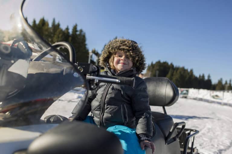 Cute boy enjoying in winter day on a snowmobile.
