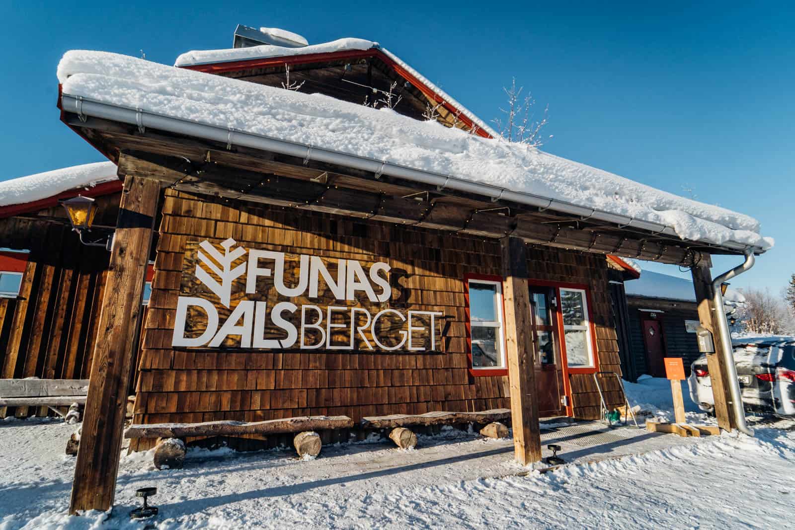 Snöklädd fjällstuga i Funäsdalen med fjällen i bakgrunden, perfekt för fjällsemester och skidåkning i Sveriges bästa skidområde.