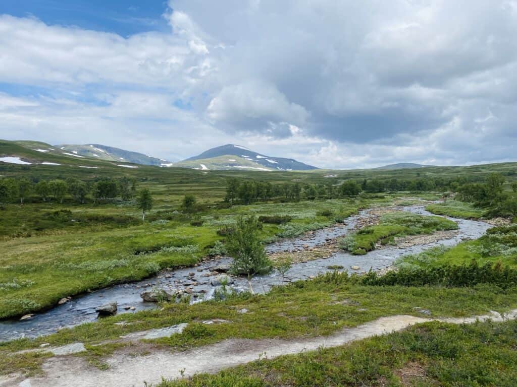 cross-river Mountain landscape in Funäsdalen with stream, green valleys and snow-covered mountains in the background, perfect for mountain vacation and skiing.